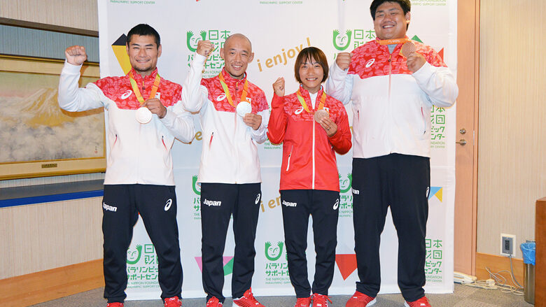 日本代表チームの4名の選手たちがパラリンピック競技大会を終えて、メダルを首に掲げてガッツポーズをしている様子